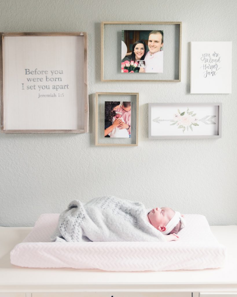 newborn baby girl on changing pad in front of wall gallery