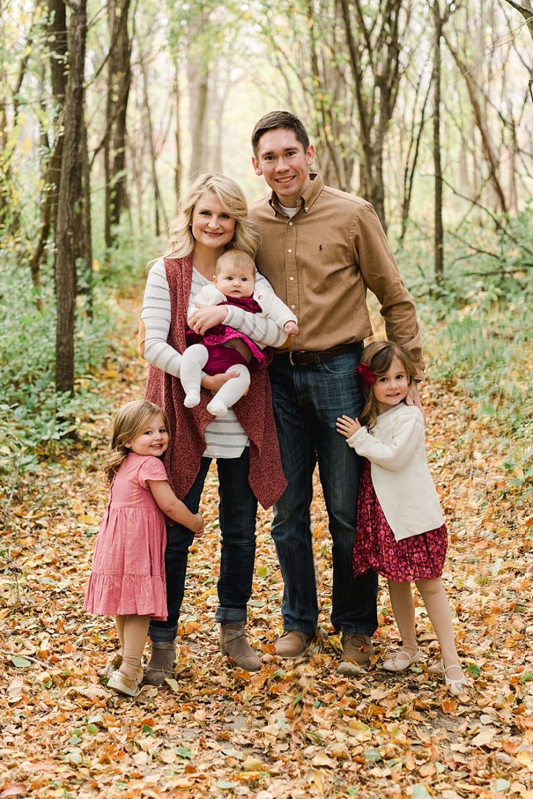 Family of Five including three little girls outdoors under a canopy of trees wearing coordinating outfits for fall