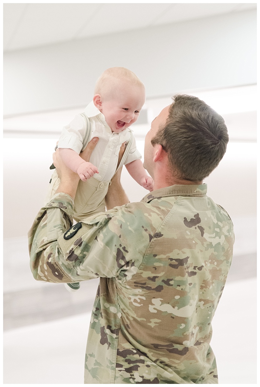daddy lifting son in the air and son is smiling after they meet for the first time at military homecoming
