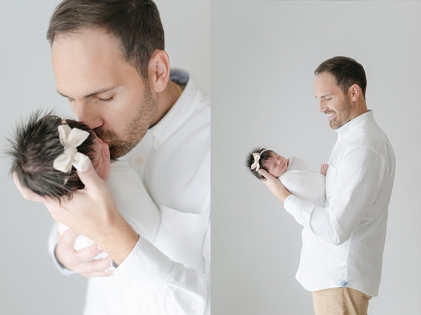 father smiling and kissing newborn baby girl in light and airy iowa city photography studio