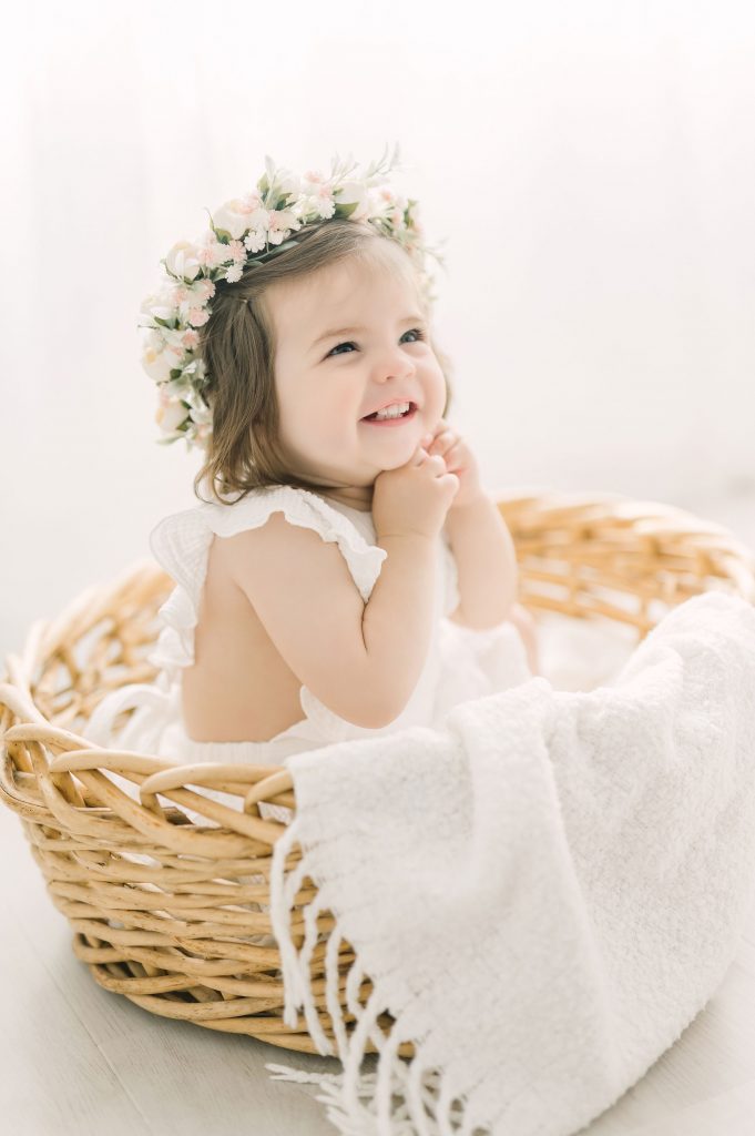 little girl wearing floral crown sitting in a basket for first birthday photos