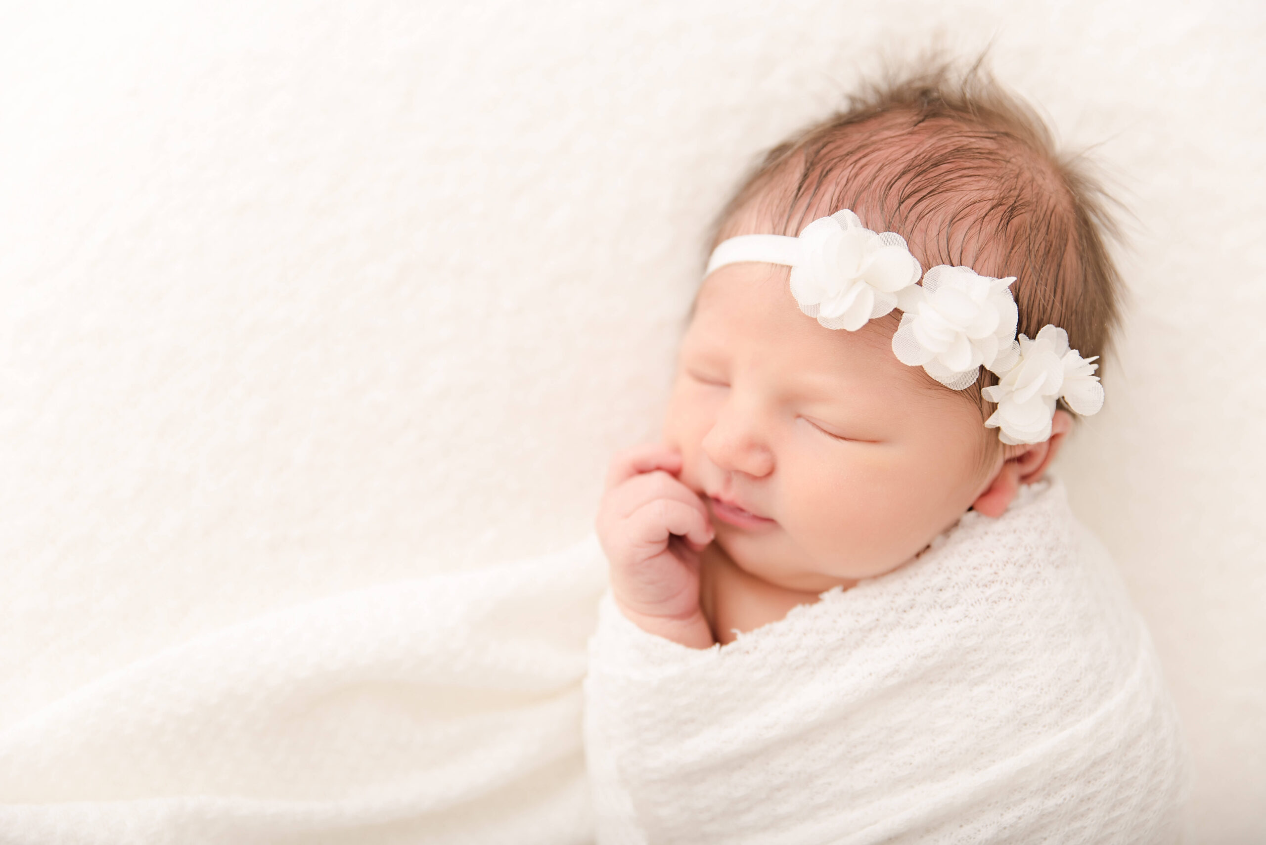 newborn baby girl swaddled in white waffle swaddle with dainty floral tulle headband