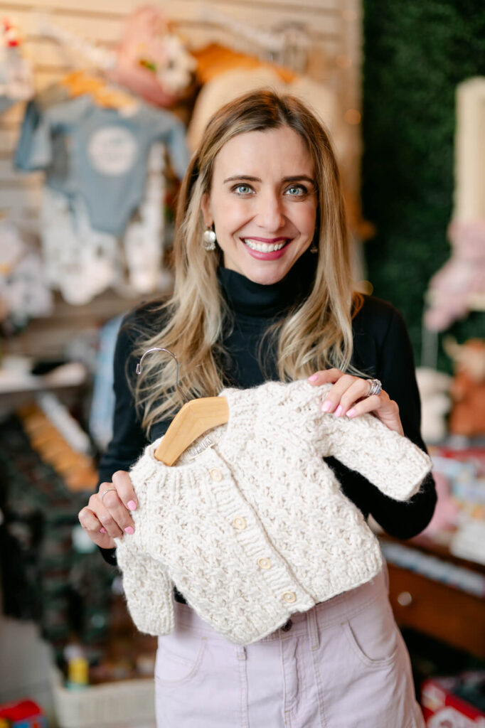 headshot of the peekaboo baby boutique owner holding up a precious knit sweater 