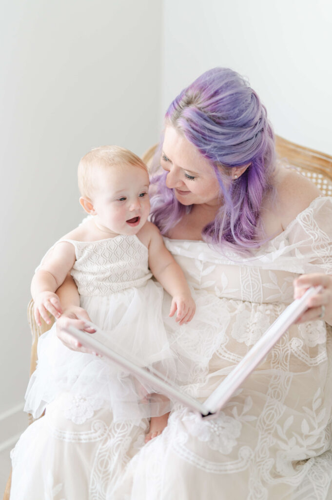 baby girl sitting on her moms lap looking through her first birthday baby album